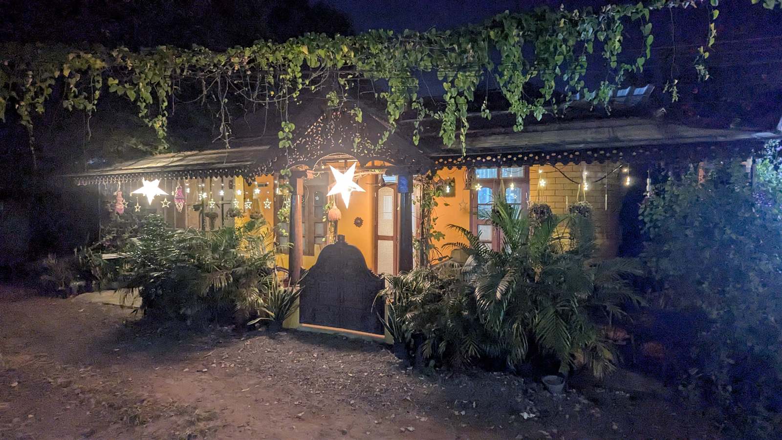 A lit-up hillside cottage at night among tropical plants