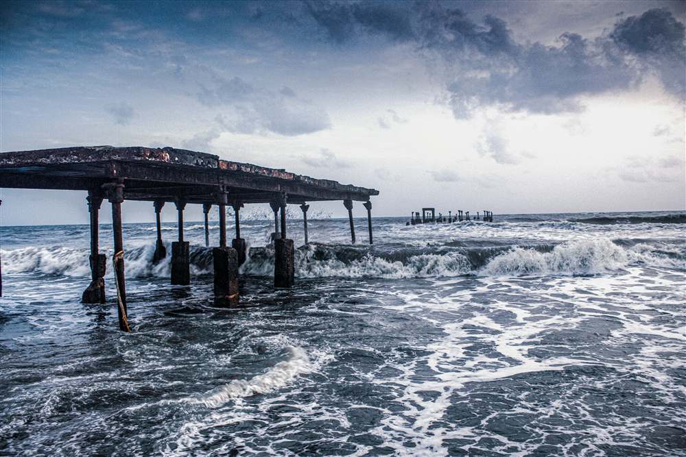 Waves breaking around an old pier on the Kerala coast under stormy skies