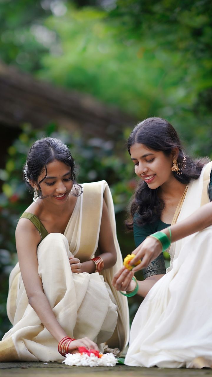 Women in Kerala kasavu sarees arranging an Onam flower carpet