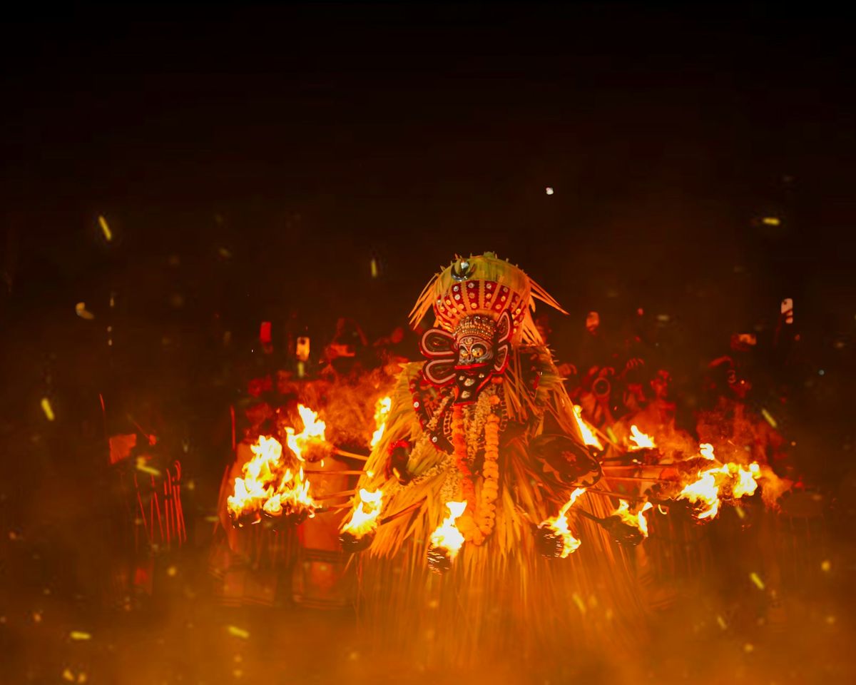 A Theyyam performer in a towering costume surrounded by flames